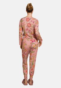 Floral gemustertes pinkes Loungewear-Set aus weichem Stoff, bestehend aus langen Ärmeln, eng anliegenden Hosen und elastischen Bündchen. Hausschuhe runden das Outfit ab.