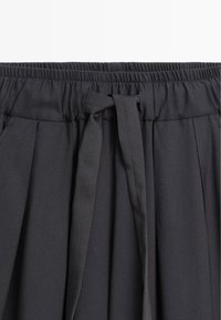 Black, pleated skirt featuring an elastic waistband and a fabric tie for adjustment. Smooth texture with no visible patterns.