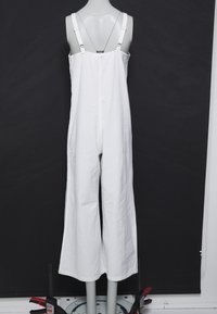 Mono de lino blanco con tirantes ajustables, diseño de pierna ancha y cierre de botones en el frente. Textura suave con acentos mínimos.