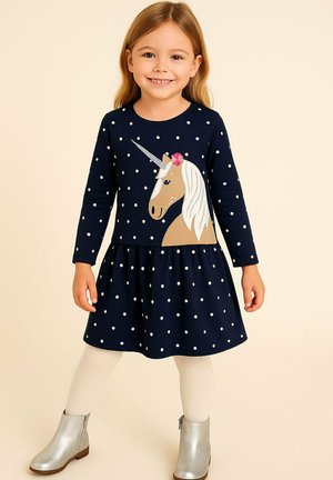 Marineblaues Polka-Dot-Kleid mit langen Ärmeln, das einen Einhornprint auf dem Oberteil und einen ausgestellten Rock hat. Kombiniert mit silbernen Ankle Boots.