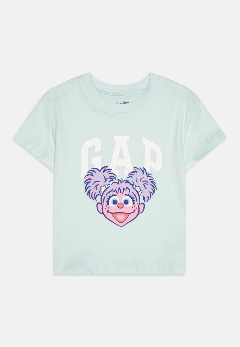 Mėtų žalios spalvos medvilninė marškinė, kurių priekyje pavaizduota veikėjo galva su violetinėmis ir rožinėmis šukuosenomis, o viršuje - baltas tekstas 'GAP'.