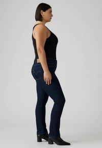 Mörkblå, slim-fit jeans med hög midja och klassisk femfickdesign. Bärs med en svart linne och svarta klackstövlar vid ankeln.