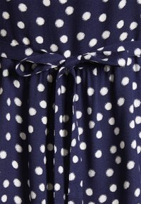Vestido de tecido azul-marinho com bolinhas brancas, apresentando um cinto atado na cintura e um acabamento suave e texturizado.