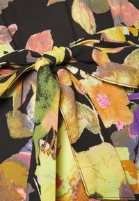 Um tecido com padrão floral apresenta cores brilhantes como amarelo, laranja, rosa e verde, com um fundo preto e um detalhe de laço amarrado.