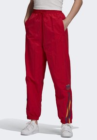 Červené, lehké joggingové kalhoty s elastickým pasem, bočními kapsami a duhovými pruhy po stranách. Logo Adidas na kotníku.