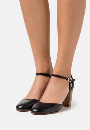 Bottines en cuir noir avec un bout rond, une sangle de cheville avec une boucle et un talon en bois texturé.