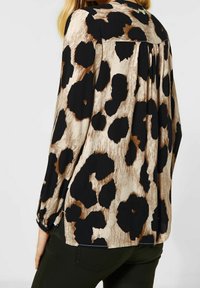 Blusa a maniche lunghe in tessuto leggero con stampa animale beige e nera, con retro plissettato e spacchi laterali per facilitare i movimenti.