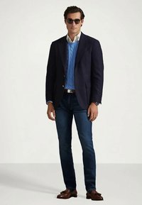 Marinblå blazer, blå kabelstickad tröja, ljusblå skjorta, mörkajeans, bruna loafers och solglasögon. Enkel design med modern passform.