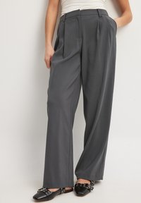 Pelēki kroku bikses, izgatavotas no gludas auduma, ar augstu jostasvietu un platām kājām, apvienotas ar melniem šauriem mokasīniem.