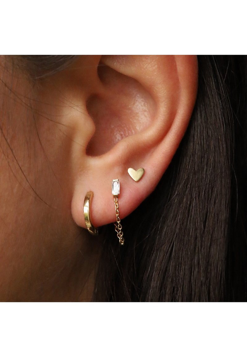 Goldene Creolen mit glatter Oberfläche, begleitet von einem goldenen Herzstecker und einem rechteckigen Kristallcharme, die durch eine feine Kette verbunden sind.