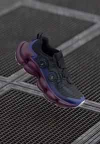 Baskets noires avec une tige texturée, des accents gris et violet, deux boutons de laçage BOA et une épaisse semelle intermédiaire violette.