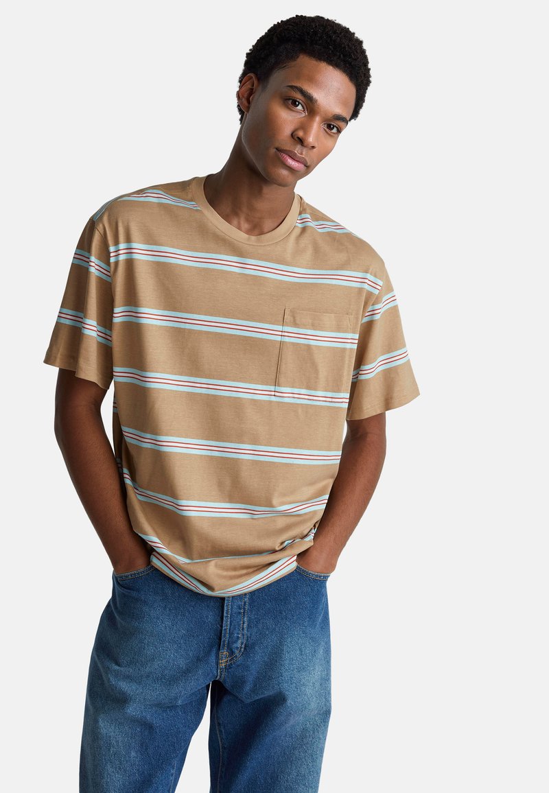 Hnědé pruhované tričko s tyrkysovými a bílými vodorovnými pruhy, krátkými rukávy, kulatým výstřihem a přední kapsou. V kombinaci s modrými džíny.