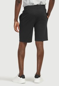 Mustat puuvillashortsit elastisella vyötäröosalla, sivutaskut ja suora leikkaus, yhdistettynä valkoisiin tennareihin, joissa on musta kantapääkorostus.