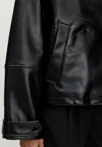 Schwarze Lederjacke mit glatter Textur, rechteckiger Tasche und Druckknopfverschlüssen an den Ärmeln. Schlichtes, tailliertes Design.