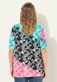 Camisa de manga corta colorida con un patrón floral en negro, turquesa y rosa. El diseño transita de un color sólido a un degradado.