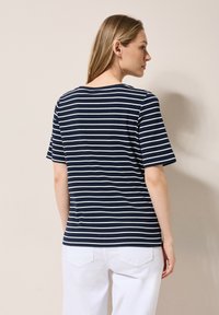 T-shirt rayé bleu marine et blanc à manches courtes, avec une encolure ronde et une coupe décontractée, porté avec un pantalon blanc. Tissu texturé.