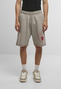 Lys grå bomulds svedshorts med elastisk talje, rød grafisk design på låret og kontrastsyning. Båret med beige sneakers.