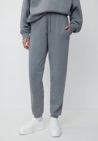 Szare spodnie dresowe z miękkiego materiału, z elastyczną talią i mankietami, wyposażone w boczne kieszenie, zestawione z białymi sneakersami.