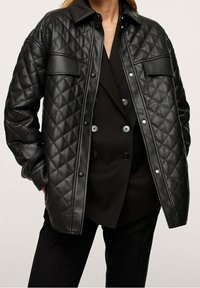 Czarna pikowana skórzana kurtka z zapięciem na guziki, dwoma kieszeniami na piersi oraz klasycznym kołnierzykiem, zestawiona z czarną dopasowaną warstwą wewnętrzną.