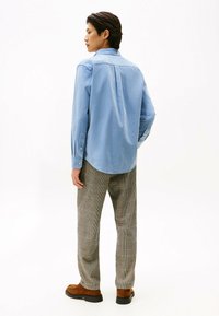 Lichtblauwe blouse met lange mouwen en een afgeronde zoom, gecombineerd met grijs geruite broeken en bruine schoenen. Glad materiaal en een aansluitend design zijn zichtbaar.