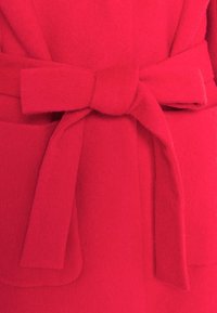 Manteau en laine rouge vif noué à la taille avec une large ceinture en tissu doux attachée en un joli nœud papillon.