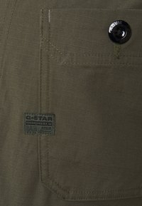 Olivgrön G-Star-jeans i tyg med texturerad yta, med en framficka, kontrasterande sömmar och en svart G-Star-logotyp.