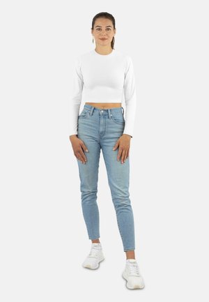 White long-sleeve cropped top paired with light blue high-waisted jeans and white sneakers. Simple design, fitted silhouette, minimal detailing.
