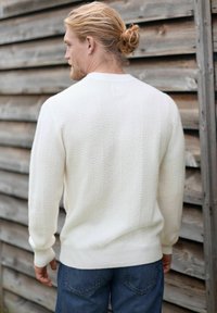 Pull en laine blanc avec un motif en zigzag, col rond et poignets côtelés, associé à un jean en denim bleu.