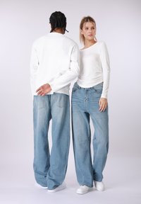 Άσπρα μακρυμάνικα πουκάμισα, ανοιχτό μπλε τζιν σε μεγάλο μέγεθος και λευκά αθλητικά παπούτσια. Το στυλ είναι χαλαρό με ορατές ραφές και τσέπες.