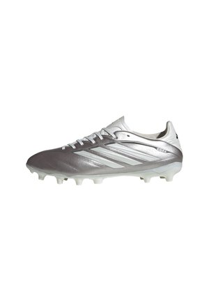 Zilveren en witte Adidas voetbalschoen met veters, drie strepen aan de zijkant en gevormde noppen voor spel op stevige ondergrond.