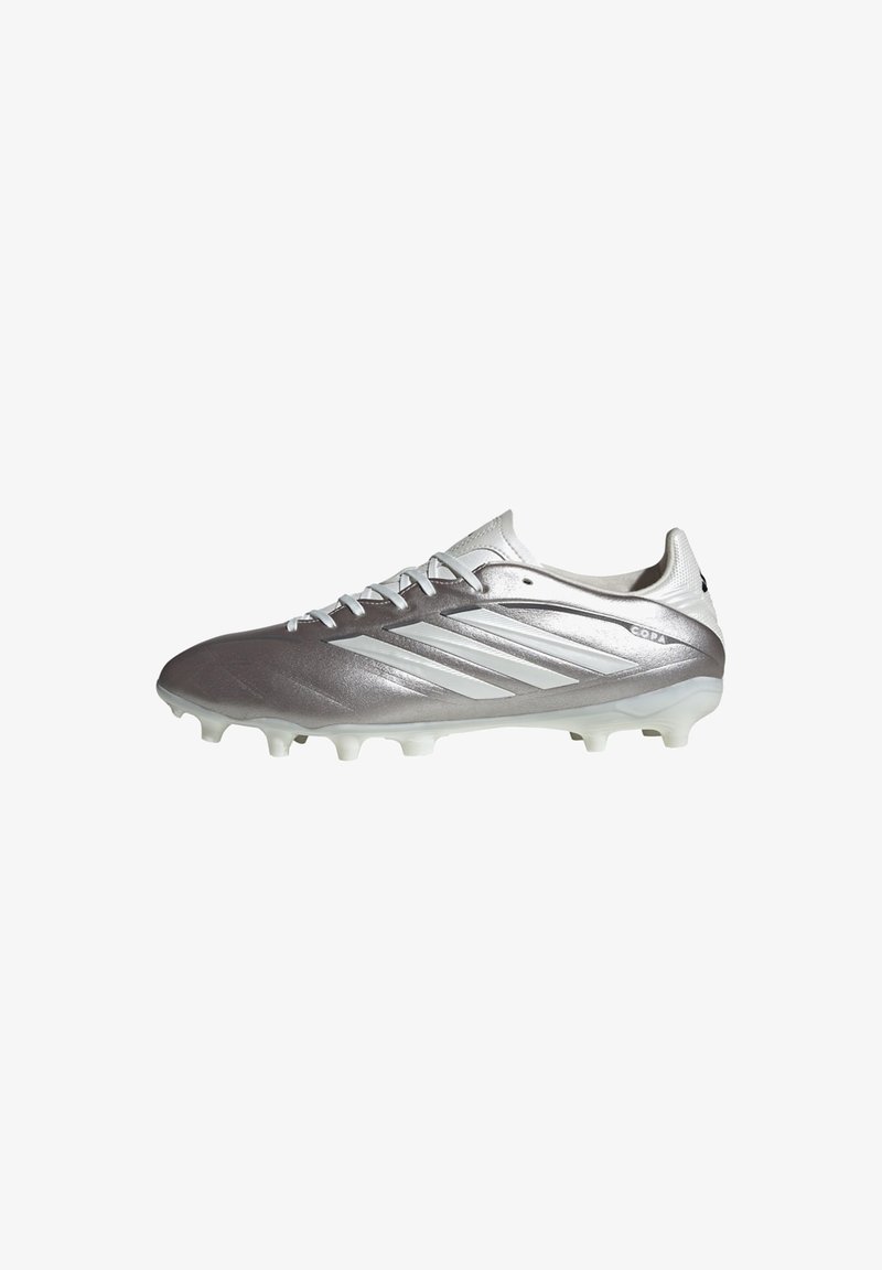 Chaussure de football Adidas argentée et blanche avec lacets, trois bandes sur le côté et crampons moulés pour jouer sur terrain ferme.