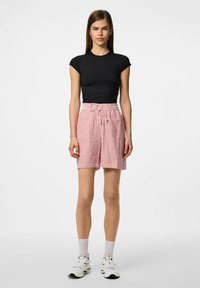 Zwarte T-shirt die strak aansluit, gecombineerd met rood-witte gestreepte shorts. De shorts hebben een elastische tailleband met een trekkenkoord. Schoeisel: witte sneakers.