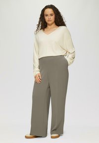 Cremfarbener V-Ausschnitt-Pullover und graue hochtaillierte weit geschnittene Hose. Der Pullover hat lange Ärmel; die Hose besitzt seitliche Taschen und eine legere Passform.