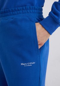 Blauwe sportieve joggers gemaakt van zacht materiaal, met een geribde tailleband en manchetten, een zijzak en het "Marc O’Polo"-logo in het wit.