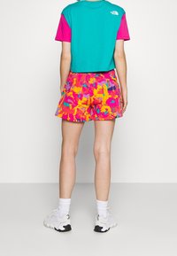 T-shirt azzurro e rosa tagliato con logo; pantaloni corte rosa con motivo colorato. Il modello indossa scarpe da ginnastica bianche e calze corte.