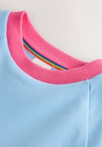 Světlá modrá látka s žebrovaným růžovým límcem a vícebarevným pruhovaným vnitřním lemováním na kusu oděvu.