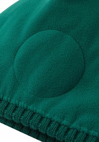 Primo piano di un tessuto in pile verde con un'area imbottita circolare e dettagli di bordo a coste.