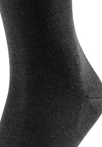 Svart strumpa av ett slätt, texturerat tyg; har en tajt passform med ribbstickade detaljer längs skaftet. Rundad tå- och hälkonstruktion.