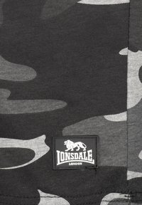 Melnā un pelēkā kamuflāžas audums ar teksturētu adījumu. Iespēlētais taisnstūra logotipa marķējums ar lauvu un tekstu "LONSDALE LONDON."