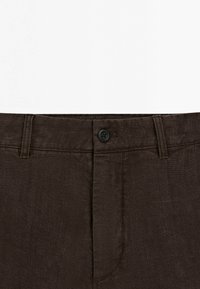 Pantalons en lin marron avec fermeture à bouton, devant plat, texture subtile et passant de ceinture standard. Aucun motif ou accent visible.