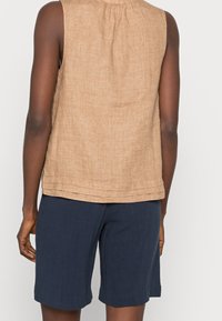 Haut sans manches en lin brun avec un col rond et un dos plissé, associé à un short bleu foncé arrivant aux genoux.