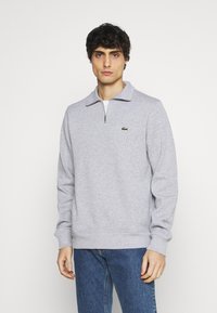 Gray sweatshirt with a zip collar, ribbed cuffs and hem, featuring a small green embroidered logo on the left chest.