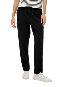 Zwarte sweatpants gemaakt van zachte stof met een elastische tailleband en een trekkoord. Voorzien van twee zijzakken, gecombineerd met witte sneakers.