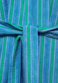 Tissu rayé bleu et vert noué en un nœud, montrant un gros plan du motif et de la texture du textile.
