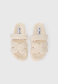 Flauschige, cremefarbene Slip-On-Sandalen mit zwei breiten Riemen und "Steve Madden"-Labels auf den Fußbetten, von oben auf einem weißen Hintergrund gezeigt.
