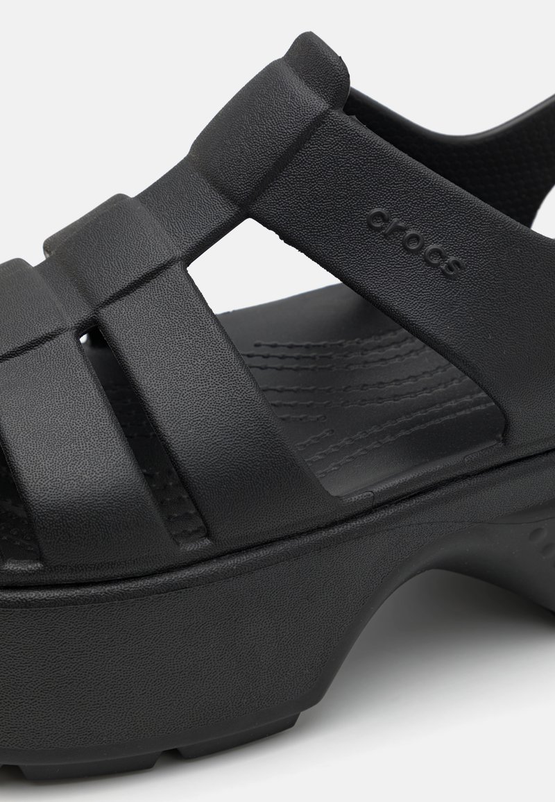 Sandalias Crocs negras con una plataforma gruesa, diseño de tiras texturizadas y talón abierto. El material parece suave y ligero.