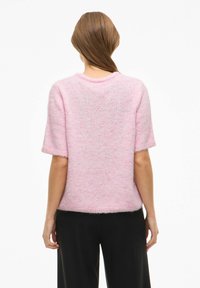 Rozā īsroku krekls no mīksta, pūkaina auduma ar apaļu kakla izgriezumu un brīvu piegriezumu, ar smalku faktūru un bez papildu detaļām.