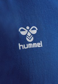 Blått tyg med en slät textur har en vit logotyp som visar en abstrakt bi-grafik med ordet "hummel" nedanför.