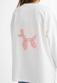 Felpa bianca con una grande grafica di un cane balloon rosa sul retro. Il design è semplice, presenta forme arrotondate e dettagli minimi.