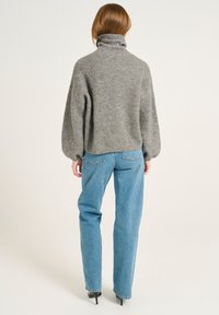 Pull en maille gris avec un col montant et des manches volumineuses, associé à un jean droit bleu clair et des chaussures à talons noires.